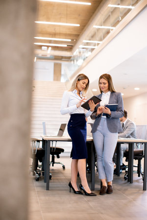 Two pretty young business women looking at financial results on digital tablet in front of their team at the officeの写真素材