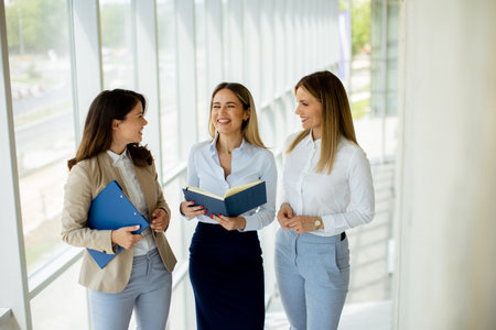 Three cute young business women having a discussion while walking in the office hallwayの写真素材