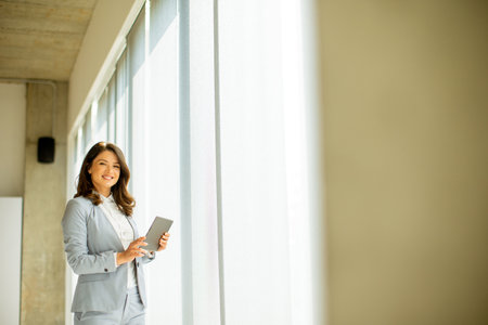 Pretty young woman working on digital tablet by the office windowの写真素材