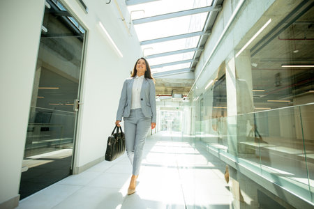 Pretty young business woman walking with briefcase in office hallwayの写真素材