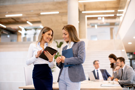 Two pretty young business women looking at financial results on digital tablet in front of their...