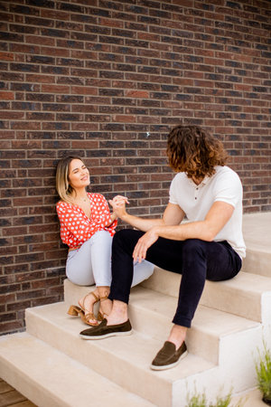 Handsome ymiling young couple in love sitting in front of house brick wallの写真素材