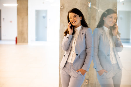 Pretty young business woman using mobile phone in the office hallway