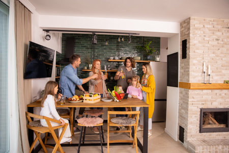 Two happy families toasting with cider while preparing dinner in the kitchenの写真素材
