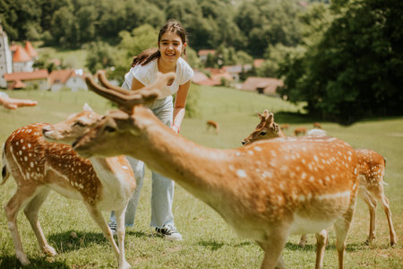 Cute little girl among reindeer herd on the sunny dayの写真素材