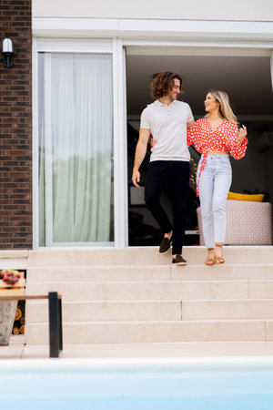 Handsome young couple walking down on stairs by the swimming pool in the house backyardの写真素材