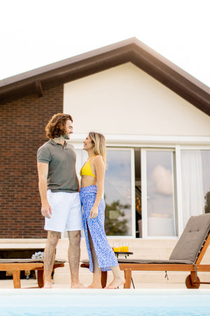 Handsome young couple relaxing by the swimming pool in the house backyard