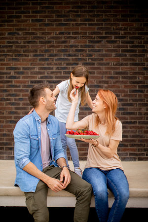Family with a mother, father and daughter sitting outside on a steps of a front porch of a brick...