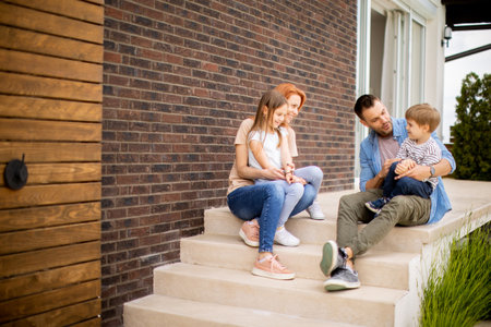 Family with a mother, father, son and daughter sitting outside on steps of a front porch of a brick houseの写真素材