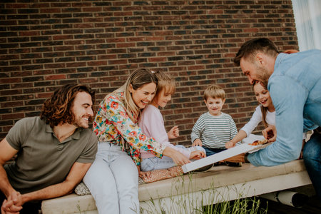 Happy group of young people and kids eating pizza in the house backyardの写真素材