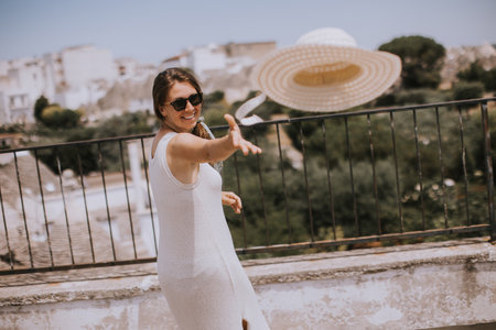 A young woman in a white dress throw hat on a sunny day during tourist visit in Alborebello, Italyの写真素材