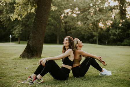 Two pretty young women sitting on the grass and relaxing after outdoor trainingの写真素材