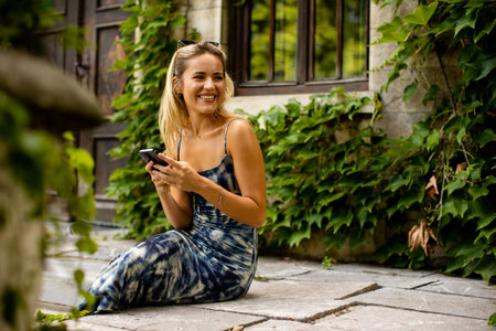 Pretty young woman using mobile phone by old house with ivyの写真素材
