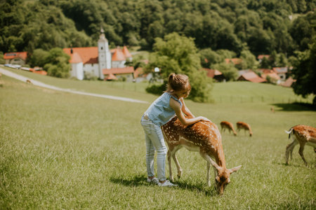 Cute little girl among reindeer herd on the sunny dayの写真素材