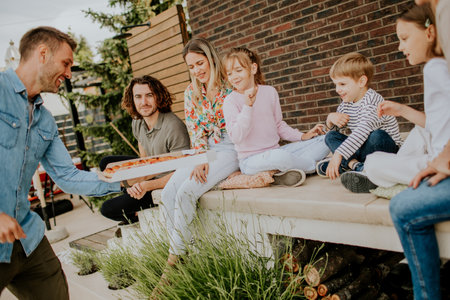 Happy group of young people and kids eating pizza in the house backyardの写真素材