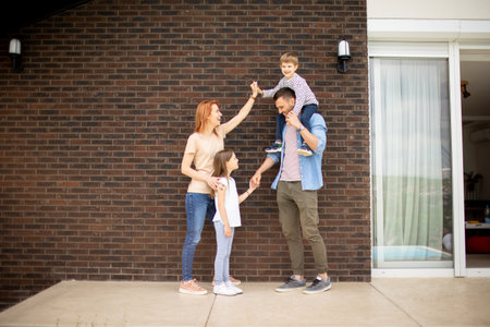 Family with a mother, father, son and daughter standing by the wall of a brick houseの写真素材