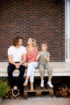 Family with a mother, father and daughter sitting outside on steps of a front porch of a brick houseの写真素材