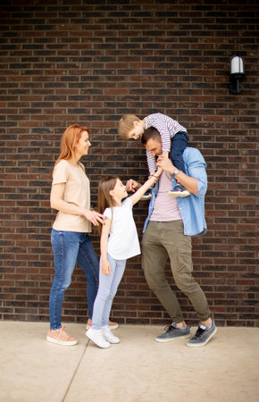 Family with a mother, father, son and daughter standing by the wall of a brick houseの写真素材