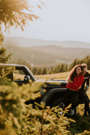 Handsome young couple relaxing by a terrain vehicle hood at countrysideの写真素材