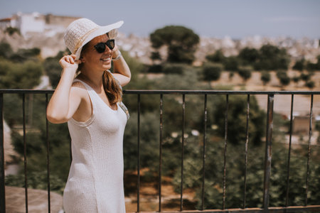 A young woman in a white dress and  hat on a sunny day during tourist visit in Alberobello, Italyの写真素材