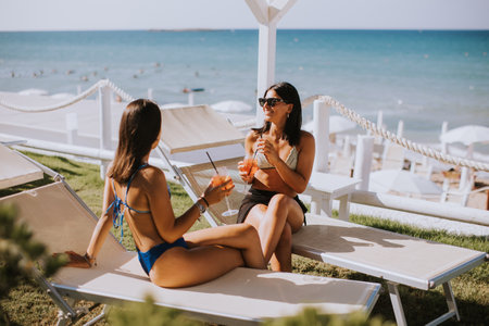 Two smiling young women in bikini enjoying vacation on the beach while drinking cocktailの写真素材