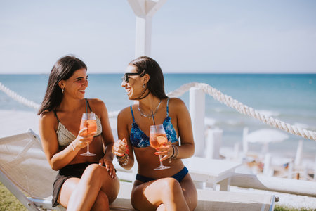Two smiling young women in bikini enjoying vacation on the beach while drinking cocktailの写真素材