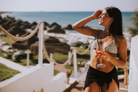 Smiling Young Woman in Bikini Enjoying Vacation on the Beach while drinking cocktailの写真素材