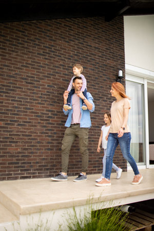 Family with a mother, father, son and daughter walking by the wall of a brick houseの写真素材