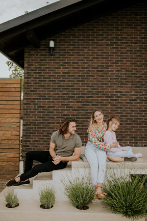 Family with a mother, father and daughter sitting outside on steps of a front porch of a brick houseの写真素材