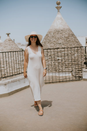 A young woman in a white dress and  hat on a sunny day during tourist visit in Alberobello, Italyの写真素材
