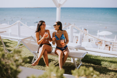 Two smiling young women in bikini enjoying vacation on the beach while drinking cocktailの写真素材