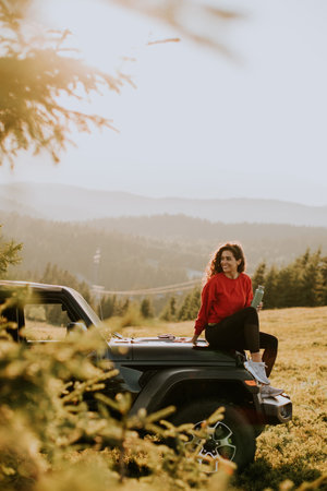 Pretty young woman relaxing on a terrain vehicle hood at countrysideの写真素材
