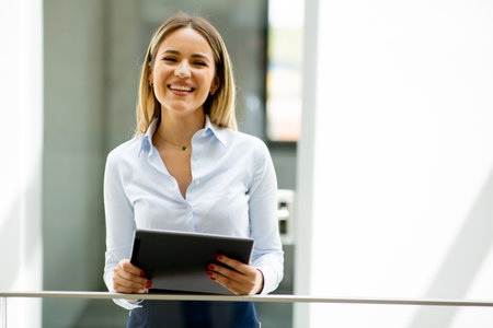 Young business woman with digital tablet standing in the modern office wallwayの写真素材