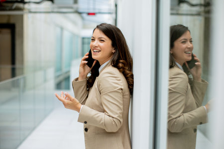 Pretty young business woman using mobile phone in the office hallwayの写真素材