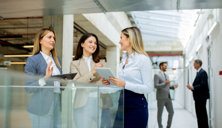 Three pretty young business women with digital tablets discussing business ideas in the office hallwayの写真素材