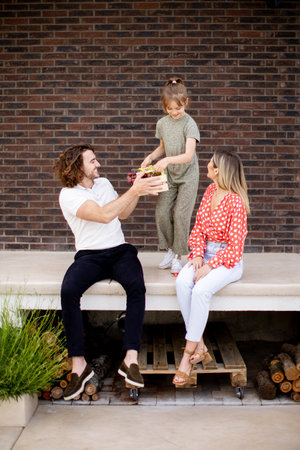 Family with a mother, father and daughter sitting outside on steps of a front porch of a brick houseの写真素材