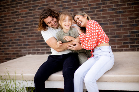 Family with a mother, father and daughter sitting outside on steps of a front porch of a brick houseの写真素材