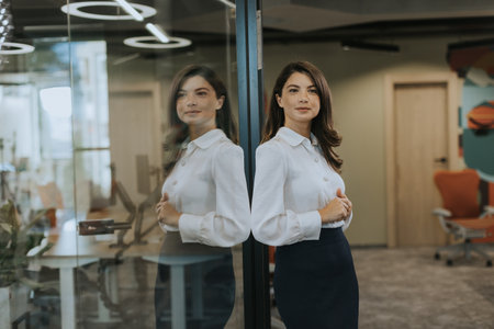 Pretty young business woman standing with arms crossed in the modern officeの写真素材
