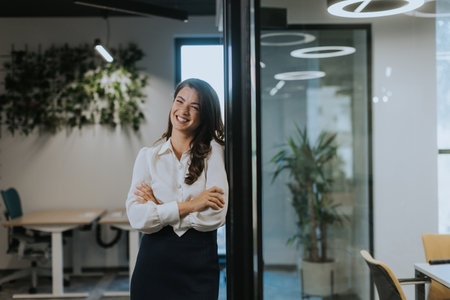 Pretty young business woman standing with arms crossed in the modern officeの写真素材