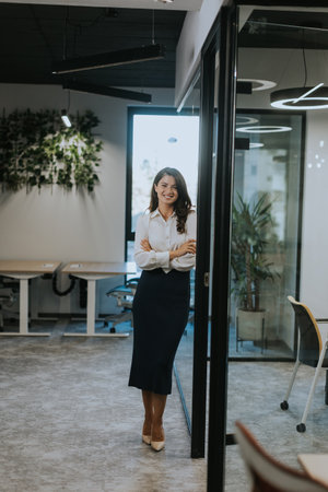 Pretty young business woman standing with arms crossed in the modern officeの写真素材