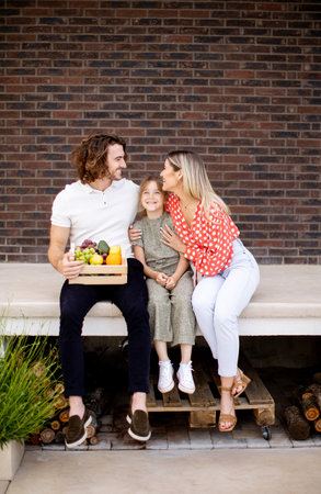 Family with a mother, father and daughter sitting outside on steps of a front porch of a brick houseの写真素材