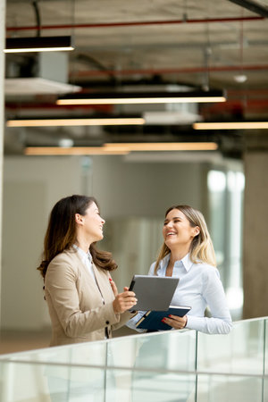 Two pretty young business women with digital tablet in the office hallwayの写真素材