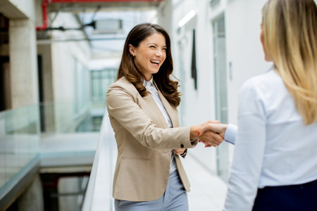 Two pretty young business women handshaking in the office hallwayの写真素材