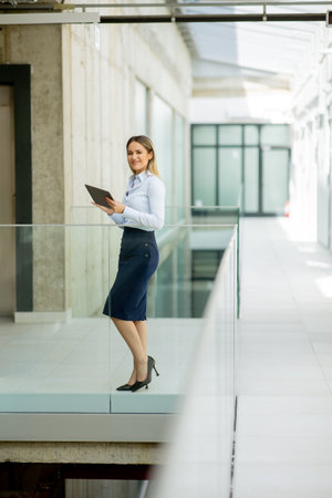 Young business woman with digital tablet walking in the modern office wallwayの写真素材