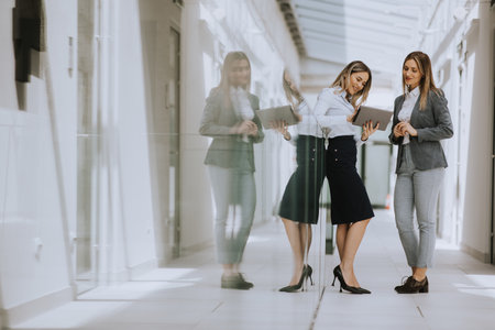 Two pretty young business women with digital tablet in the office hallwayの写真素材