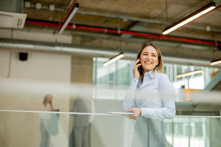 Young business woman with notebook using mobile phone and standing in the modern office wallwayの写真素材