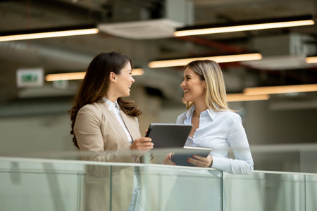 Two pretty young business women with digital tablet in the office hallwayの写真素材