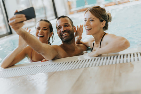Handsome young people relaxing in the indoor swimming pool and taking selfie with mobile phoneの写真素材