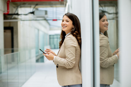 Pretty young business woman using mobile phone in the office hallwayの写真素材