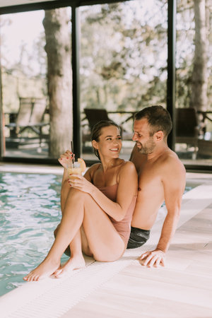 Handsome young couple relaxing by the indoor swimming poolの写真素材